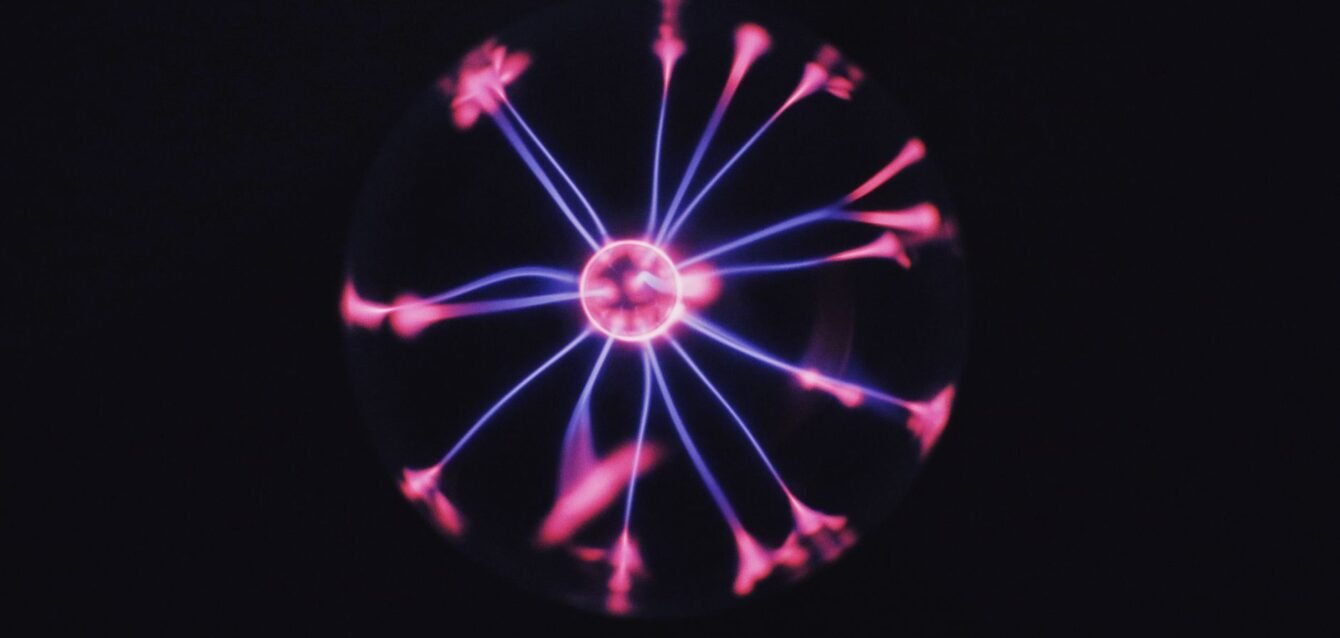 Transparent glass plasma ball with bright neon luminous against dark background in room