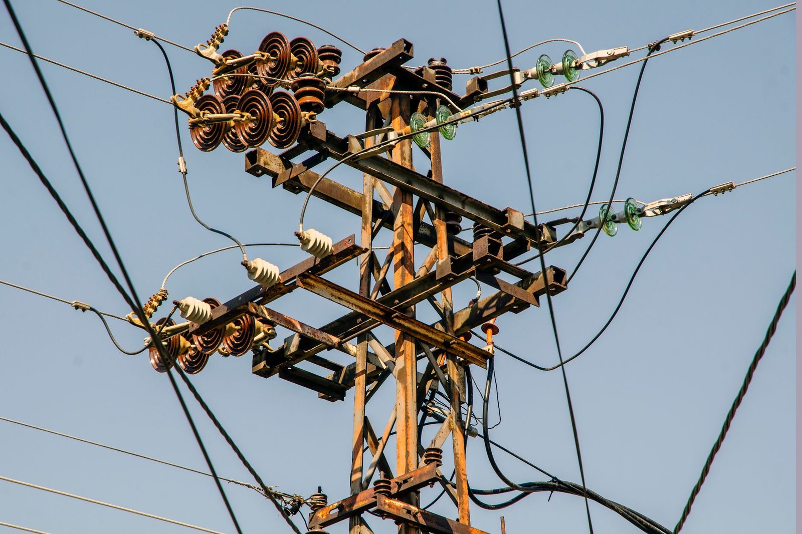 Close-up of a rustic utility pole and transmission lines against a clear sky.