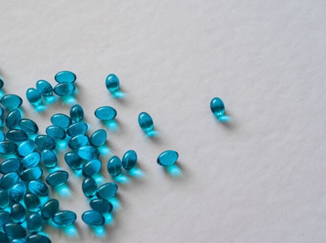 High angle view of scattered blue gel capsules on a flat white surface.