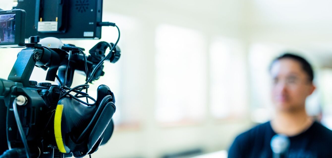 header-video-camera-interview-setup-34518758 Professional video camera setup focusing on an interview with blurred subject in the background.